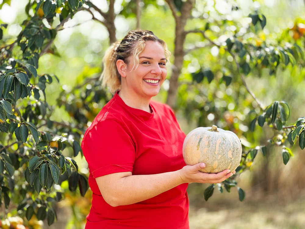Valentina sorridente con in mano una zucca davanti a degli alberi
