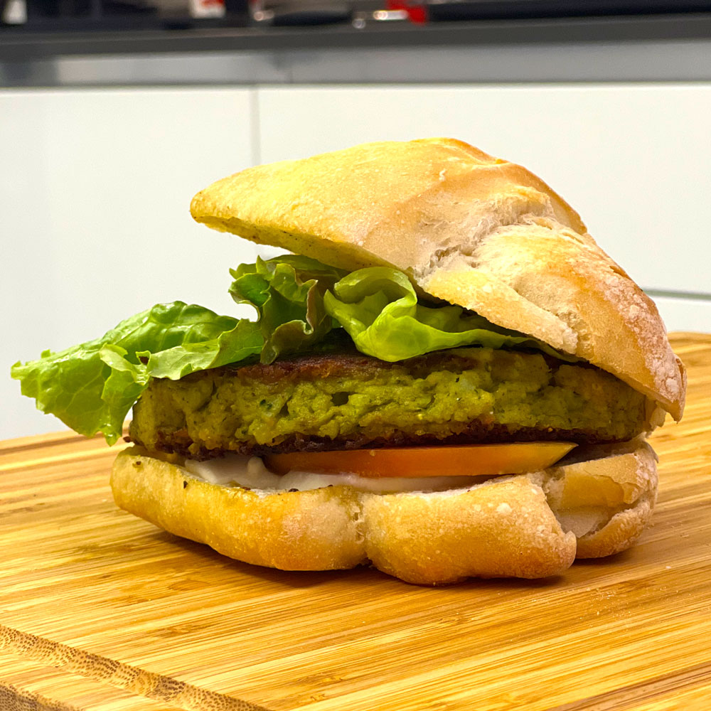 Panino con hamburger di broccolo, pomodoro e insalata su tagliere di legno