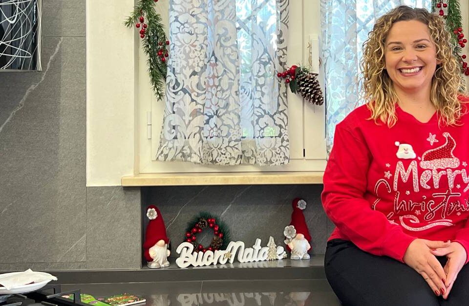 Ragazza con maglia rossa natalizia seduta sul banco della cucina addobbata