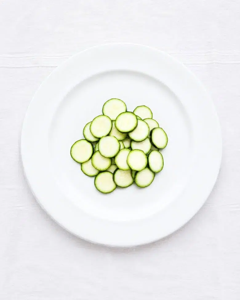 foto dall'altro di zucchine a rondelle su piatto bianco e tovaglia bianca