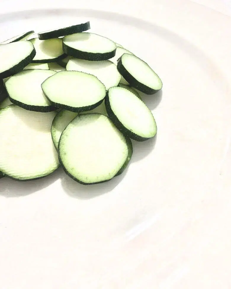 particolare di zucchine a rondelle su piatto bianco e tovaglia bianca
