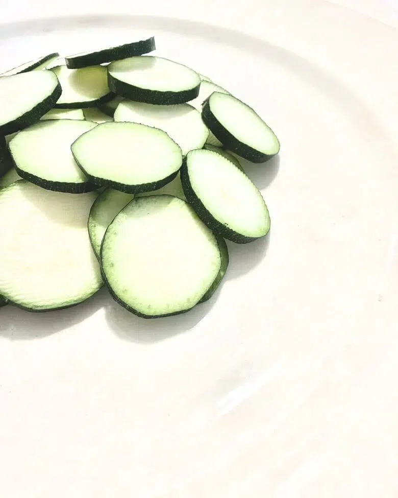 particolare di zucchine a rondelle su piatto bianco e tovaglia bianca